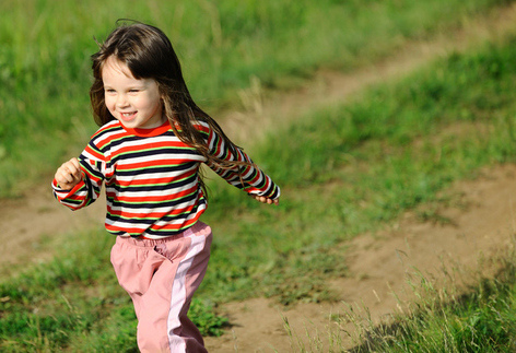 Leende tjej springer på gräs.
