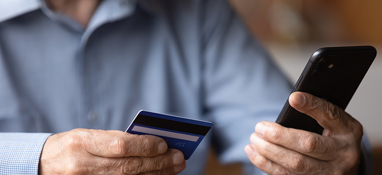 Äldre man som håller i en mobiltelefon och ett bankkort.