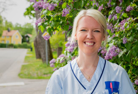 Sjuksköterska står framför en syrénbuske.