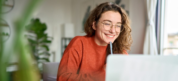 En glad kvinna som sitter och arbetar med datorn. 